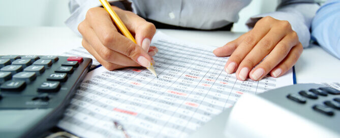 Businesswoman calculating figures on a printed financial spreadsheet with a pencil and calculator. Woman computing ATO Tax debt