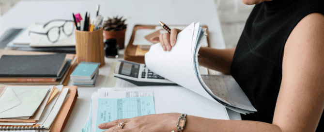 Business owner sorting through receipts and paperwork with a calculator at a desk. DIY Accounting